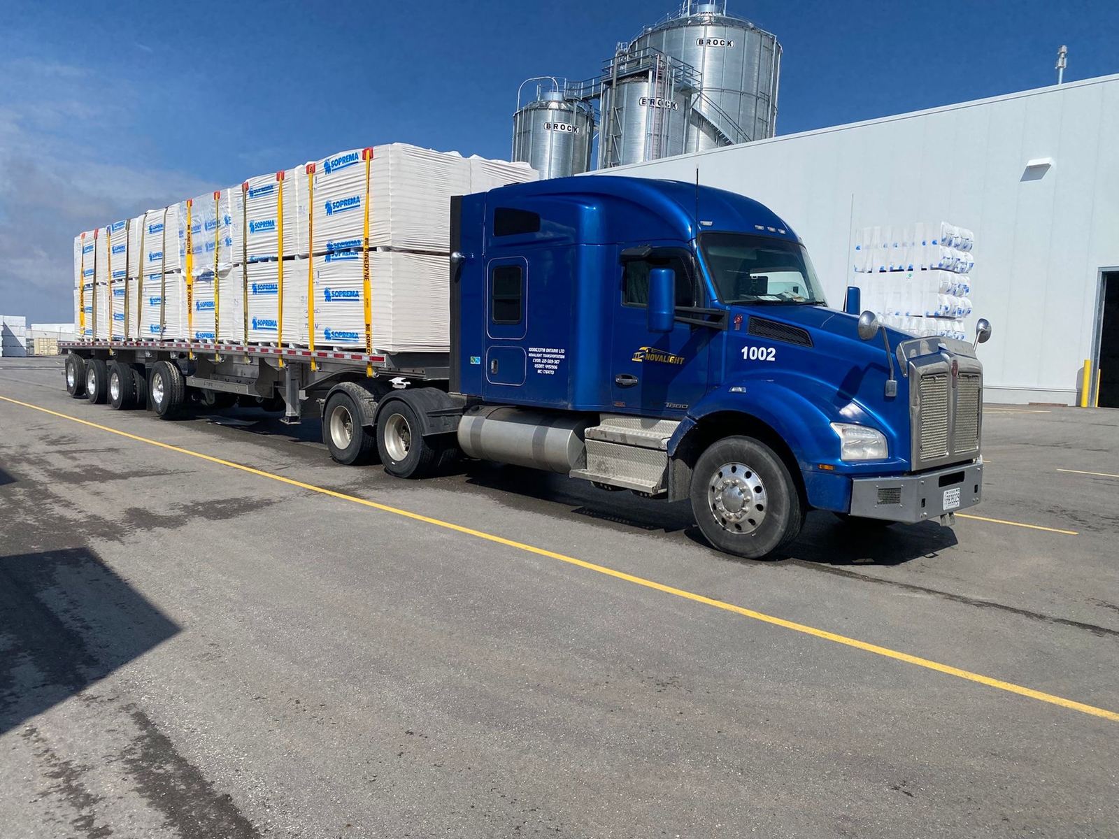 Novalight blue tractor hauling a flatbed of building materials
